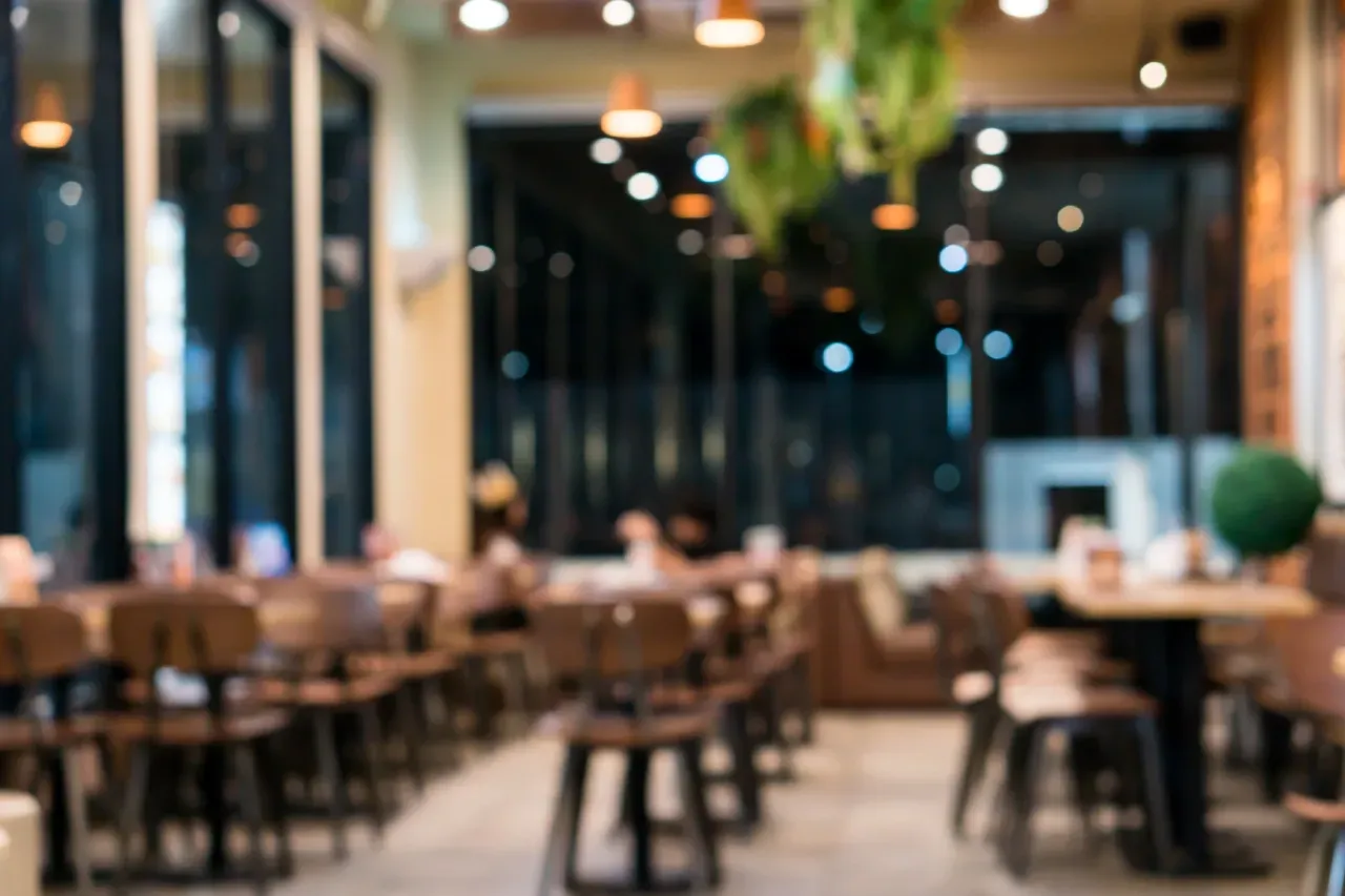 Interior desfocado de restaurante moderno com mesas e iluminação aconchegante.