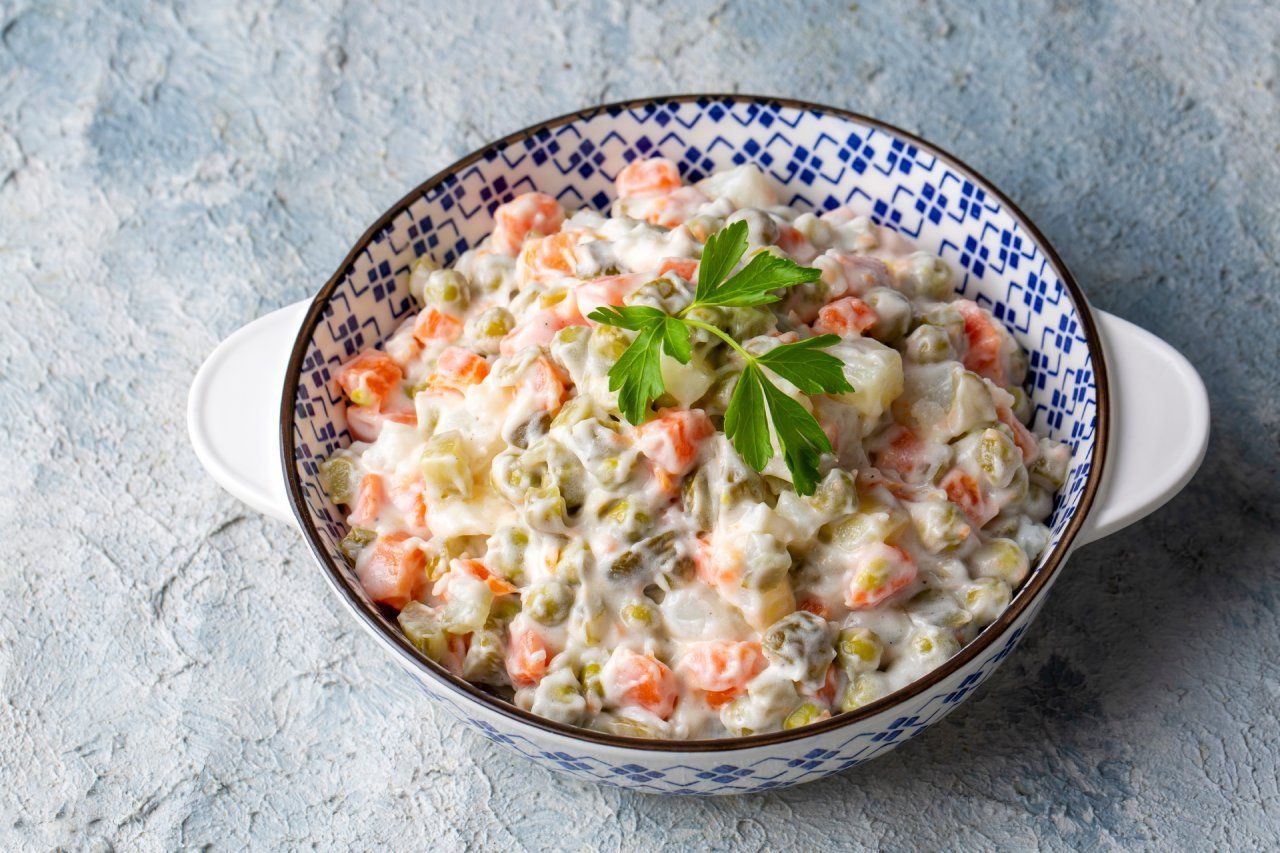 Uma tigela de salada maionese com cenouras, ervilhas e maionese sobre uma mesa.