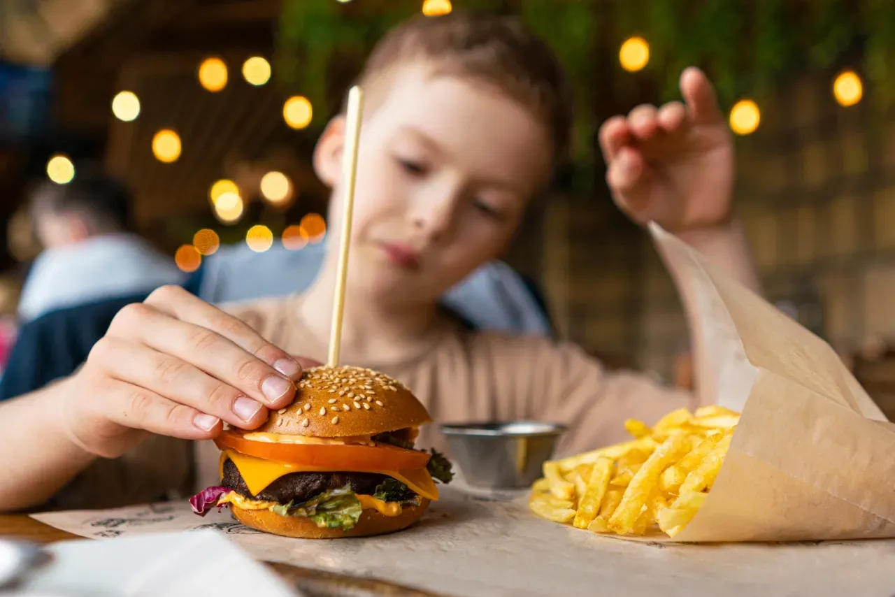 Criança segurando um hambúrguer com batatas fritas em restaurante.