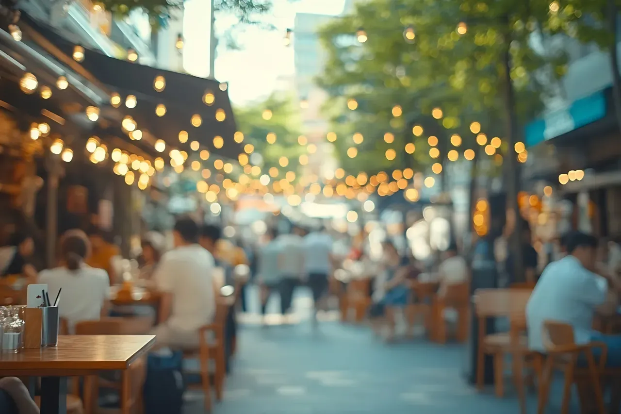 pessoas comendo em um restaurante com mesas na rua e iluminação suspensa