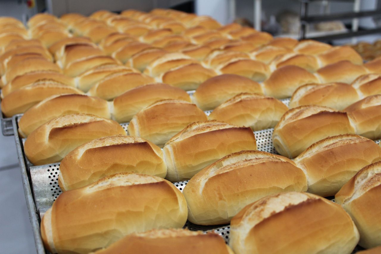 Um monte de pãezinhos estão em uma bandeja em uma padaria.