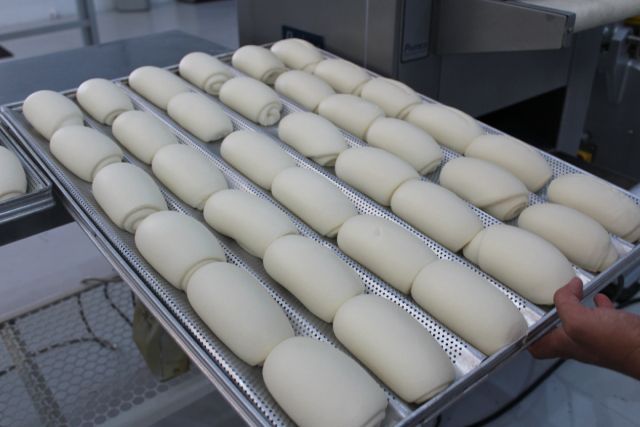 Uma pessoa está segurando uma bandeja de pãezinhos de massa