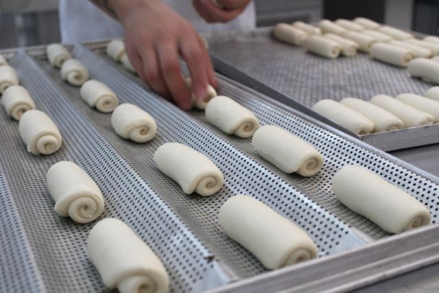 Uma pessoa está rolando massa em uma bandeja perfurada