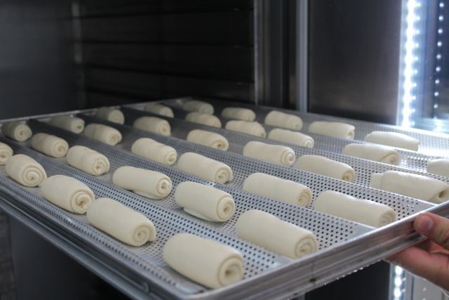 Uma pessoa está tirando uma bandeja de pãezinhos do forno.