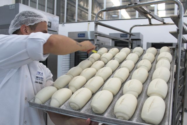 Um homem segura uma bandeja de massa em uma padaria