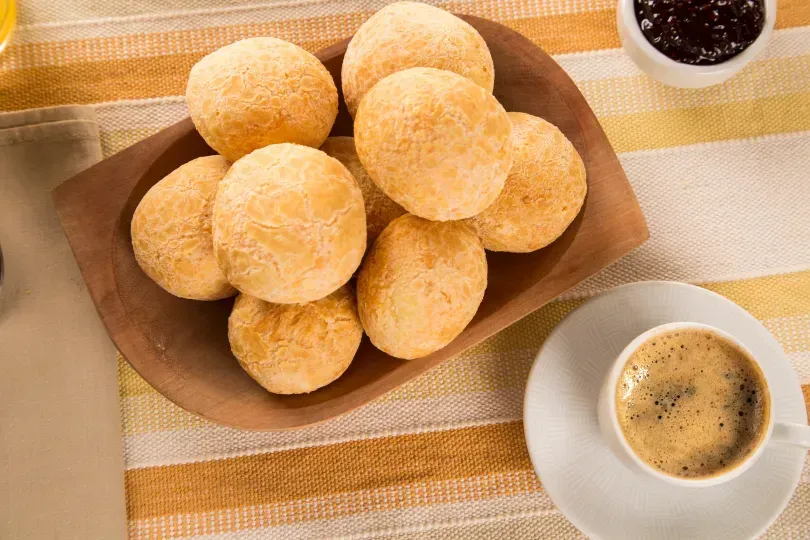 pães de queijo assados em vasilha de madeira com xícara de café ao lado