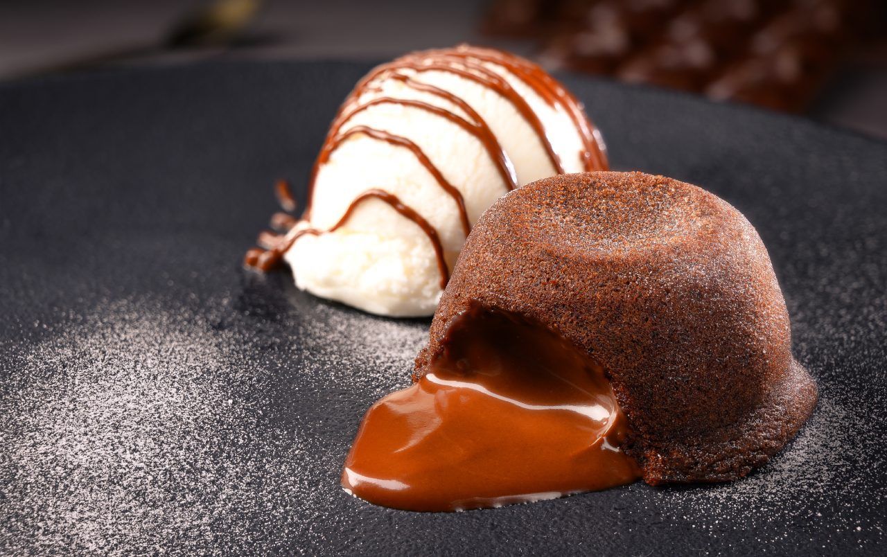 Um bolo de chocolate com sorvete e calda de chocolate em um prato preto.