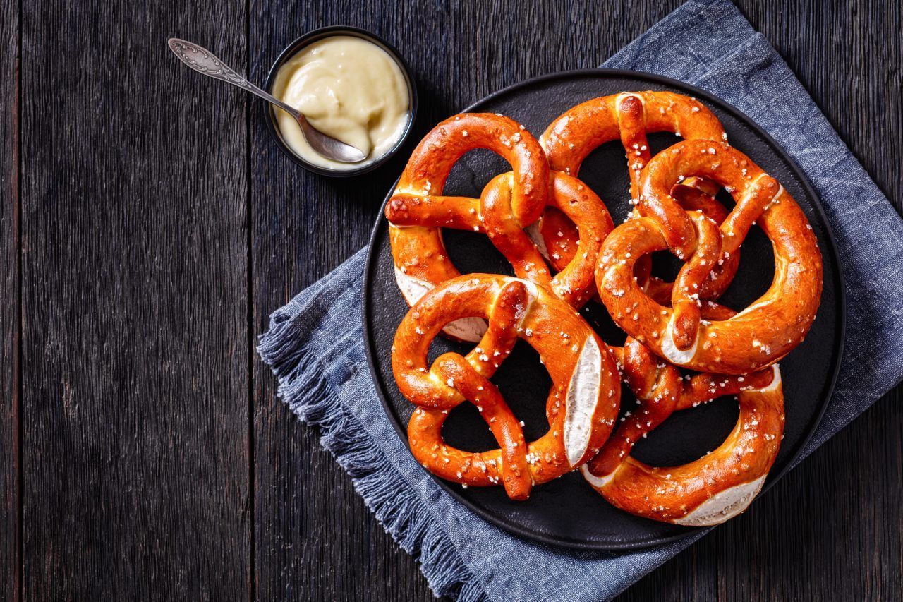 Um prato de pretzels com mostarda sobre uma mesa de madeira.