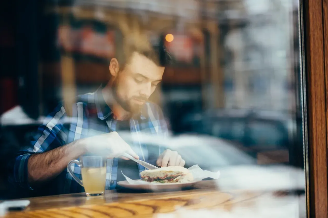 Um homem está sentado à mesa de um restaurante comendo um sanduíche.