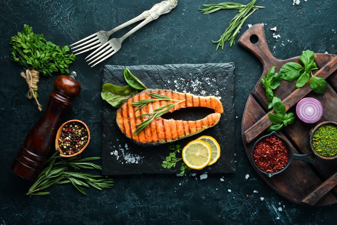 Um bife de salmão grelhado em uma tábua de corte com vegetais e temperos.