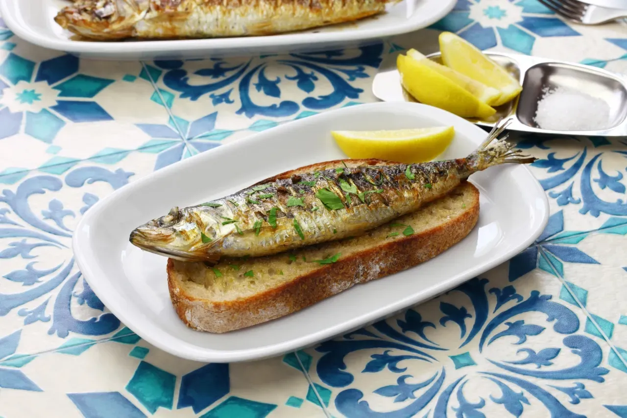 Um prato azul coberto com sardinhas e tomates em uma mesa de madeira.