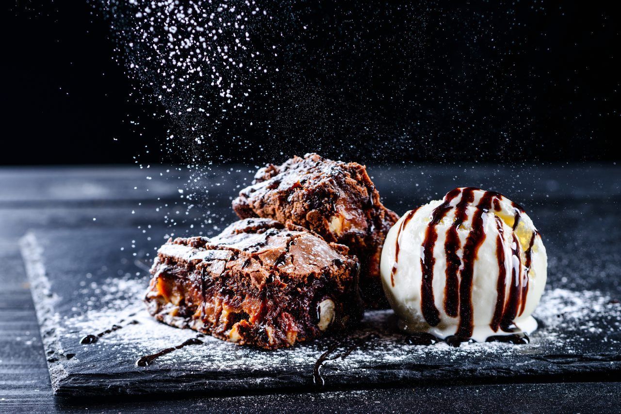 Um brownie e uma bola de sorvete com calda de chocolate em uma tábua de corte.