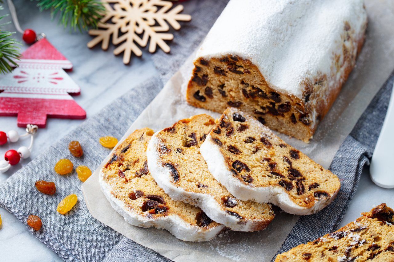 stollen de frutas coberto com açúcar de confeiteiro e fatiado com decoração de natal ao fundo