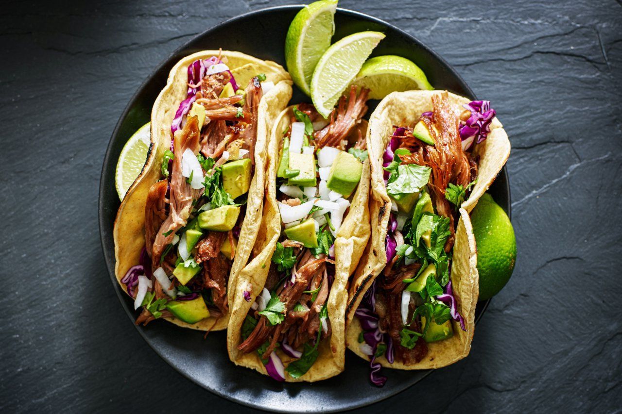 Um prato preto coberto com três tacos e fatias de limão.