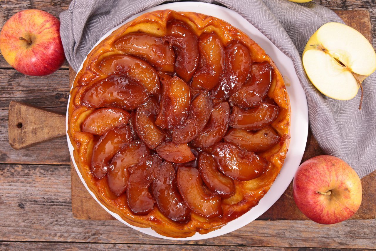 Uma torta de maçã está sobre uma mesa de madeira ao lado de maçãs.