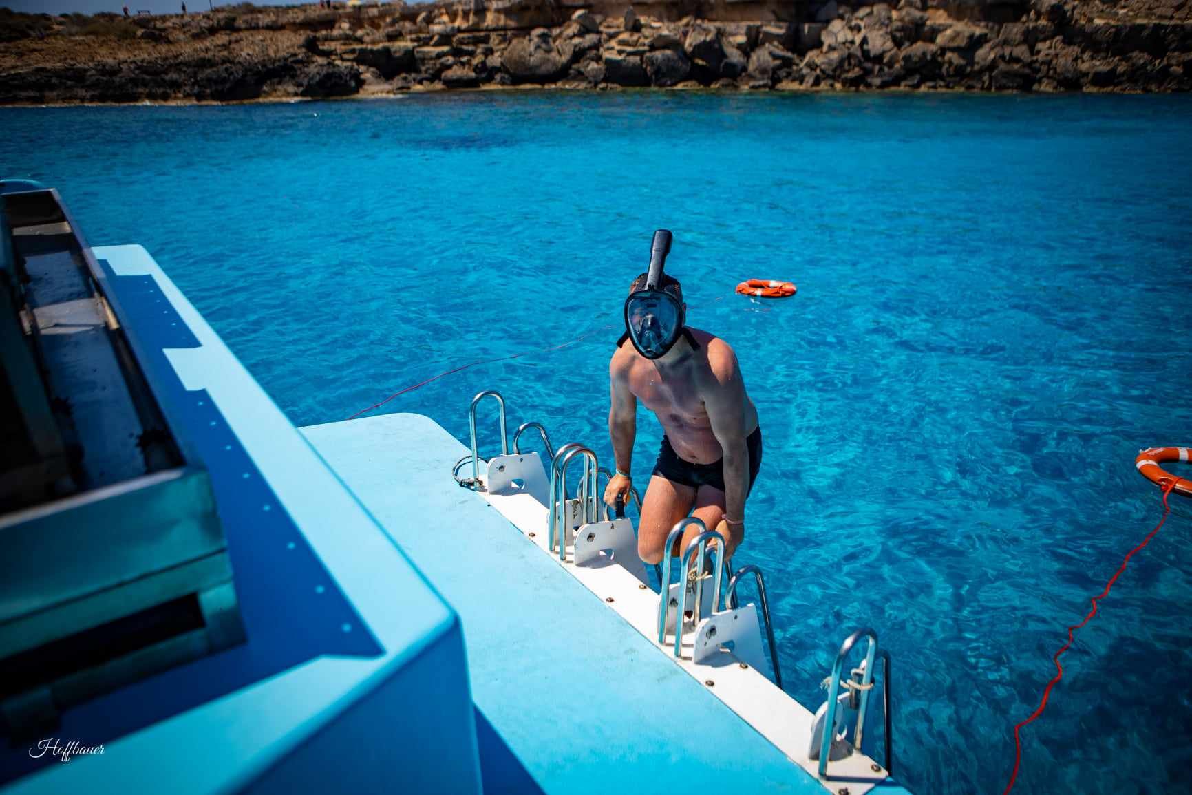 A man is standing on the side of a boat in the ocean.