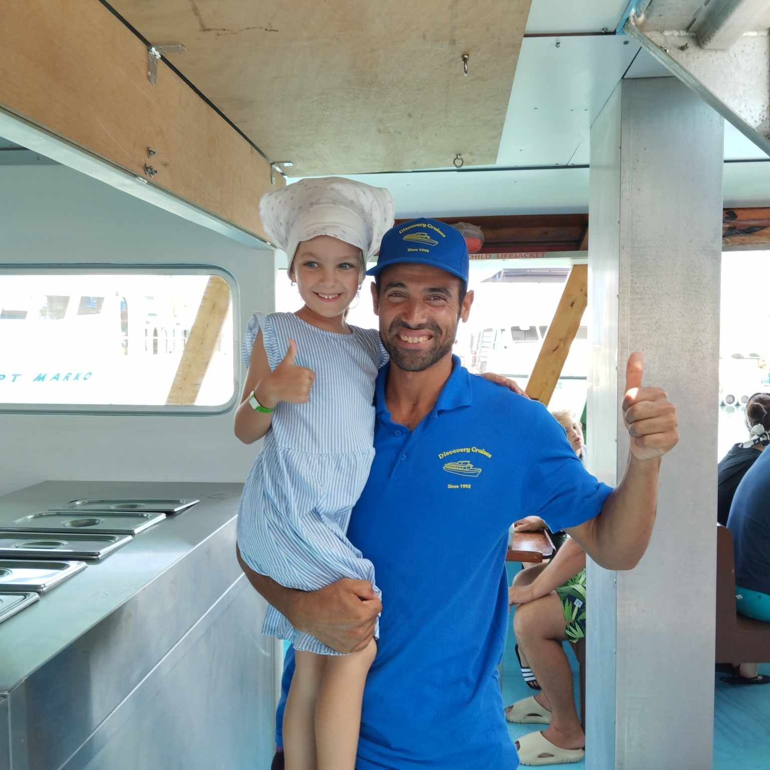 A man in a blue shirt is holding a little girl and giving a thumbs up