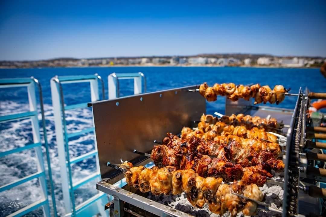 A grill filled with meat is cooking on a boat in the ocean.