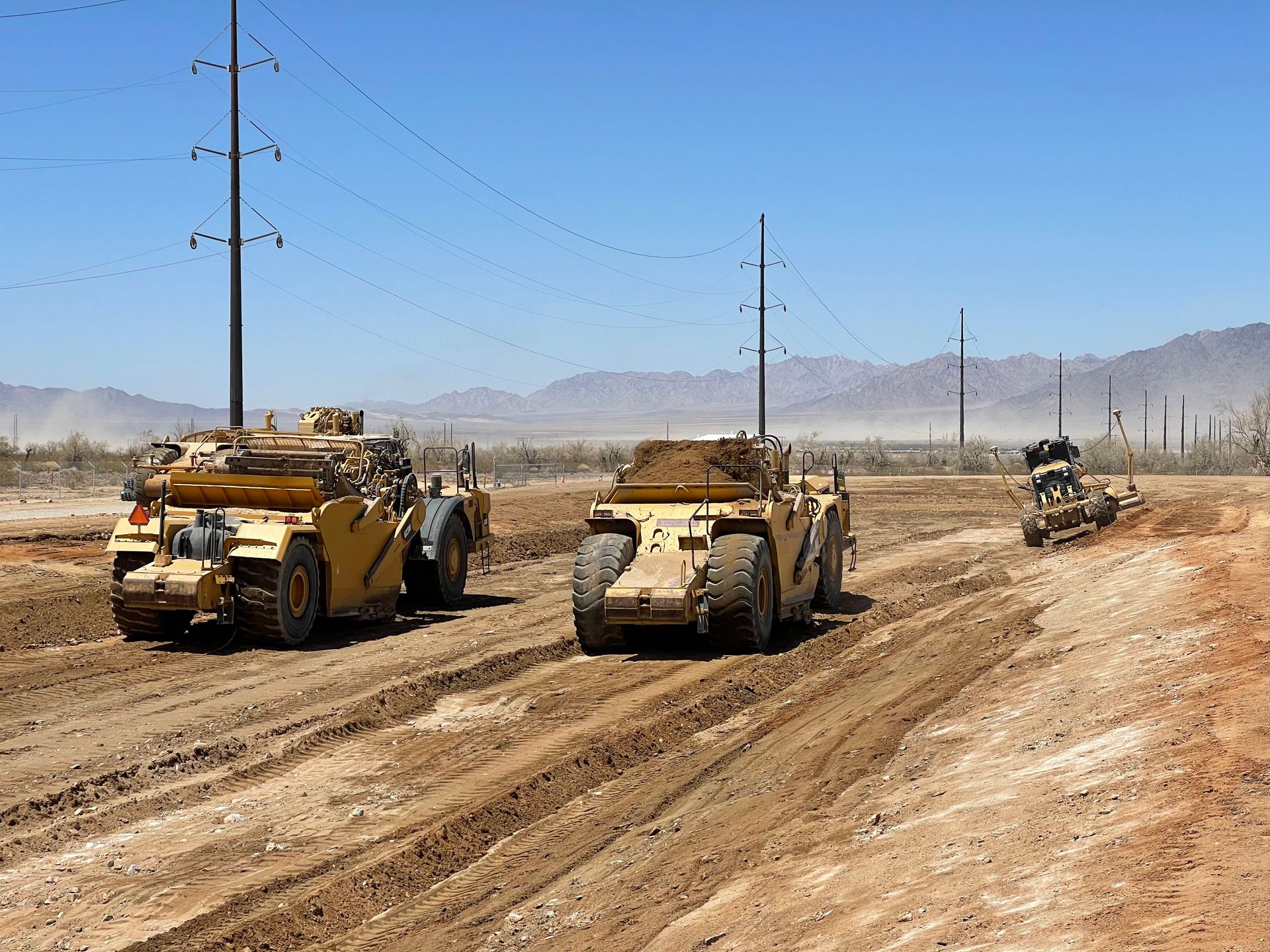 A group of construction vehicles are driving down a dirt road.