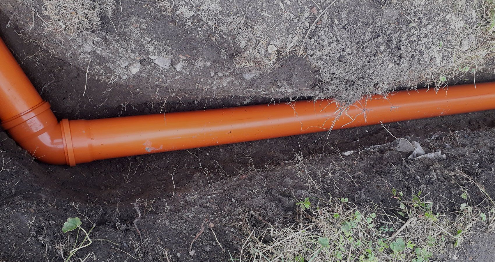 A red pipe is laying in the dirt on the ground.