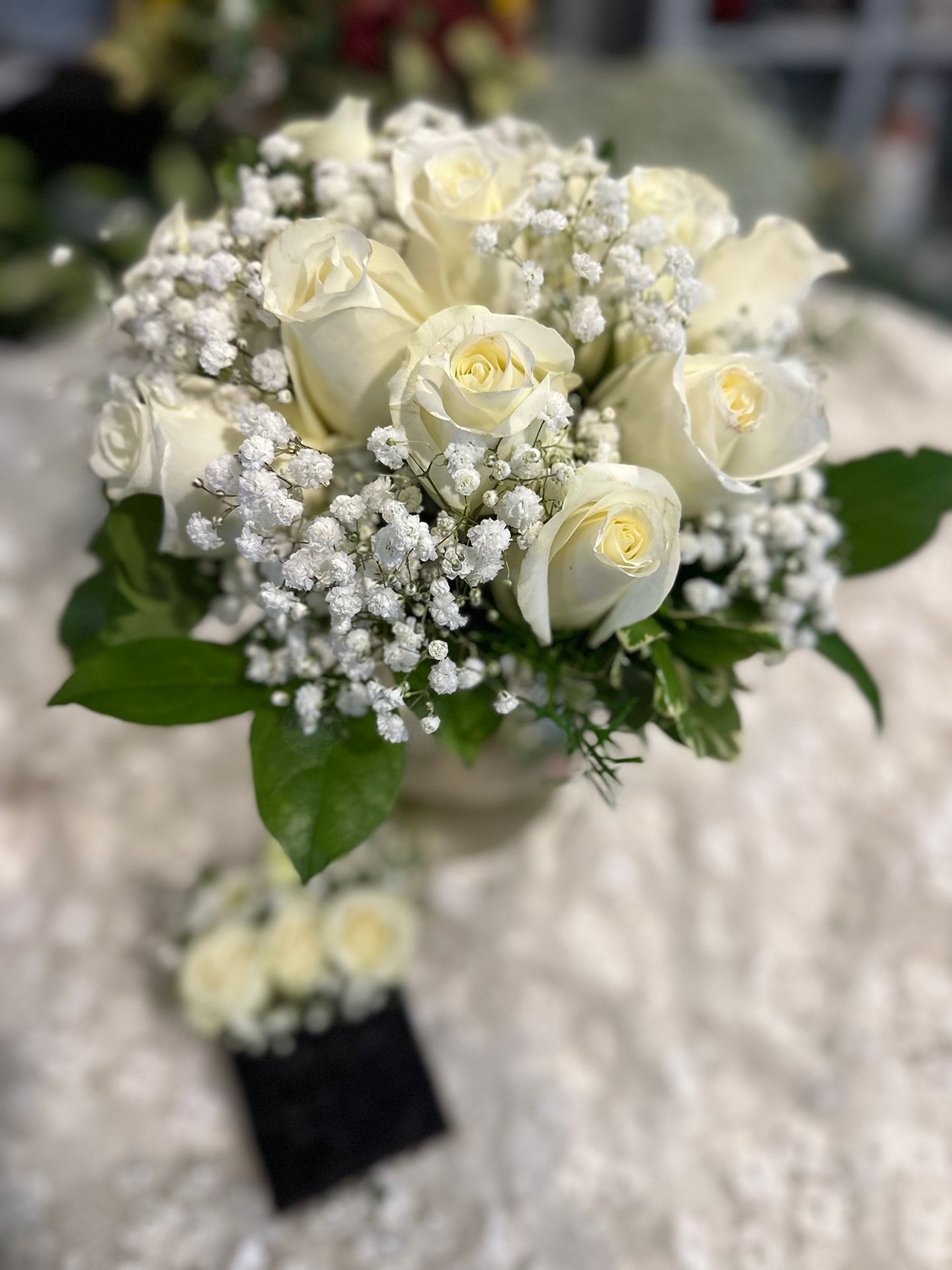Bridal bouquet of white roses and baby 's breath and corresponding pocket boutonniere is sitting on a table.