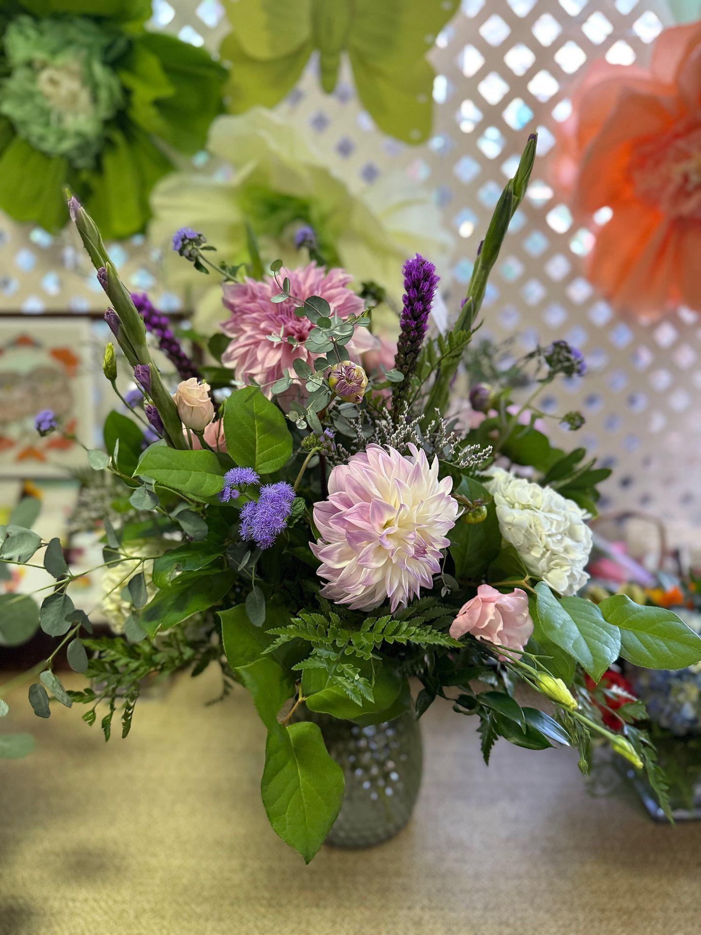 Floral arrangement in a glass vase; pink, white, purple flowers, green foliage.