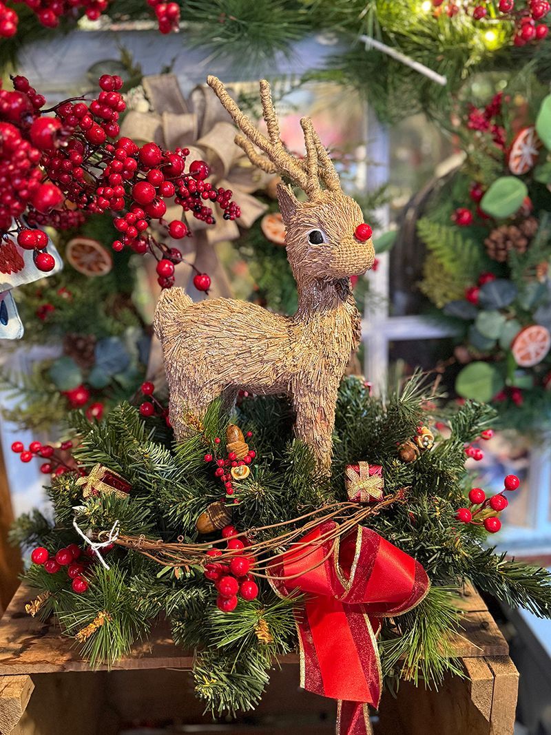 Wreath arrangement with a reindeer figure, red bow, and berries.