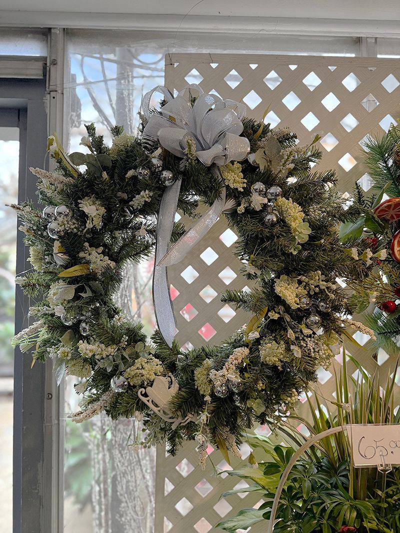 Evergreen wreath with white accents and bow, hanging in front of a white latticework.