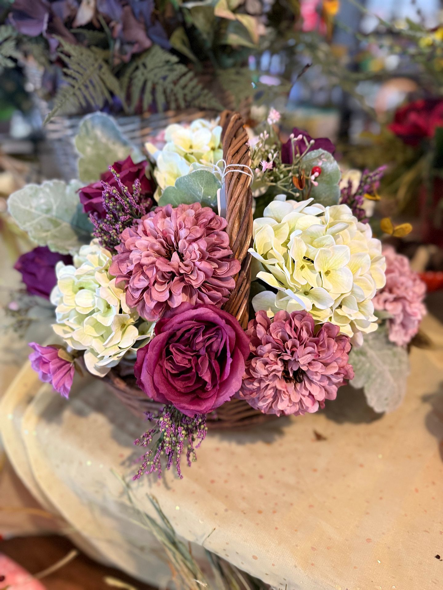 Basket of pink, white, and burgundy flowers on a tan surface.