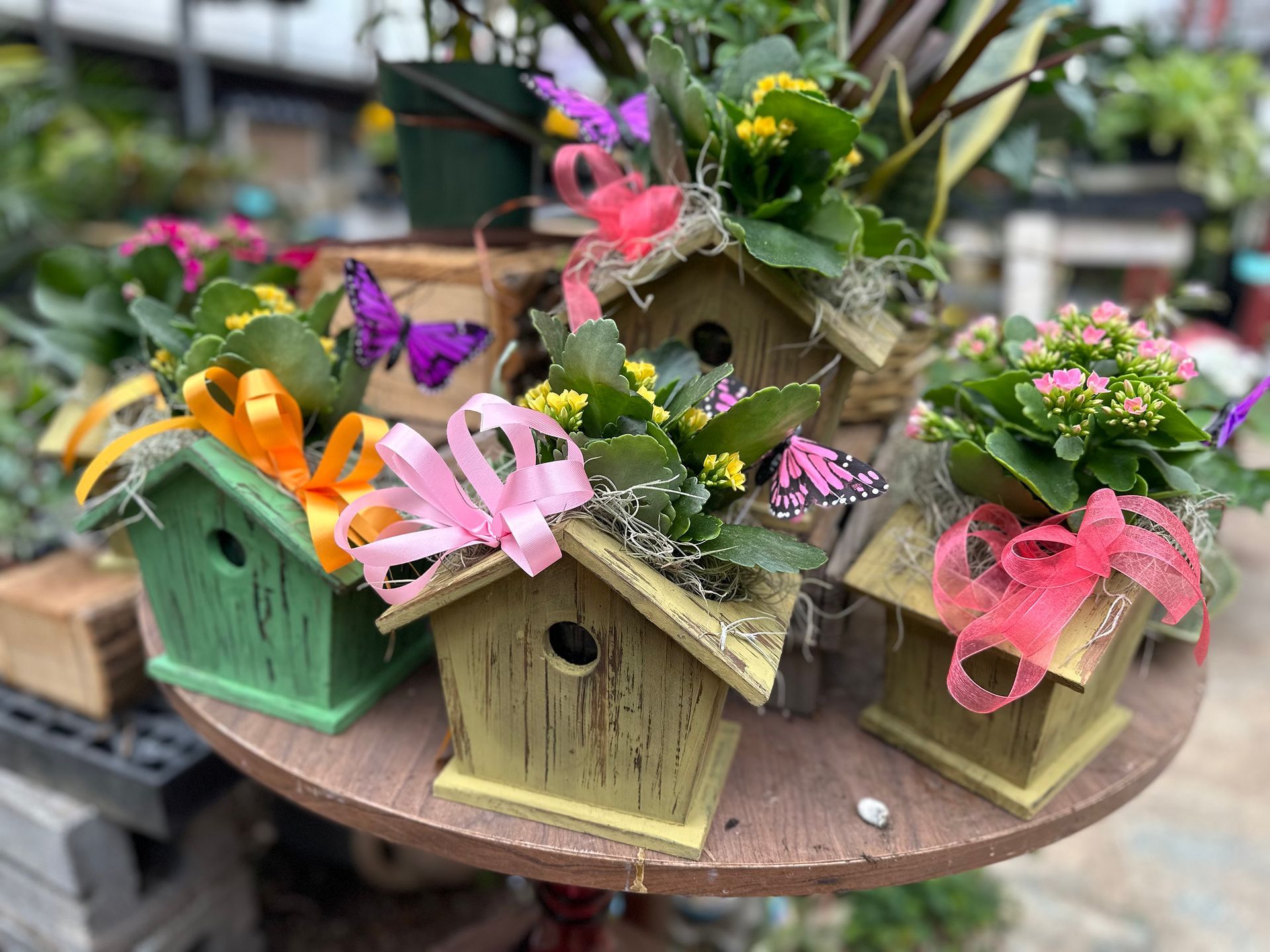 A wooden birdhouse filled with flowers and ribbons on a table.