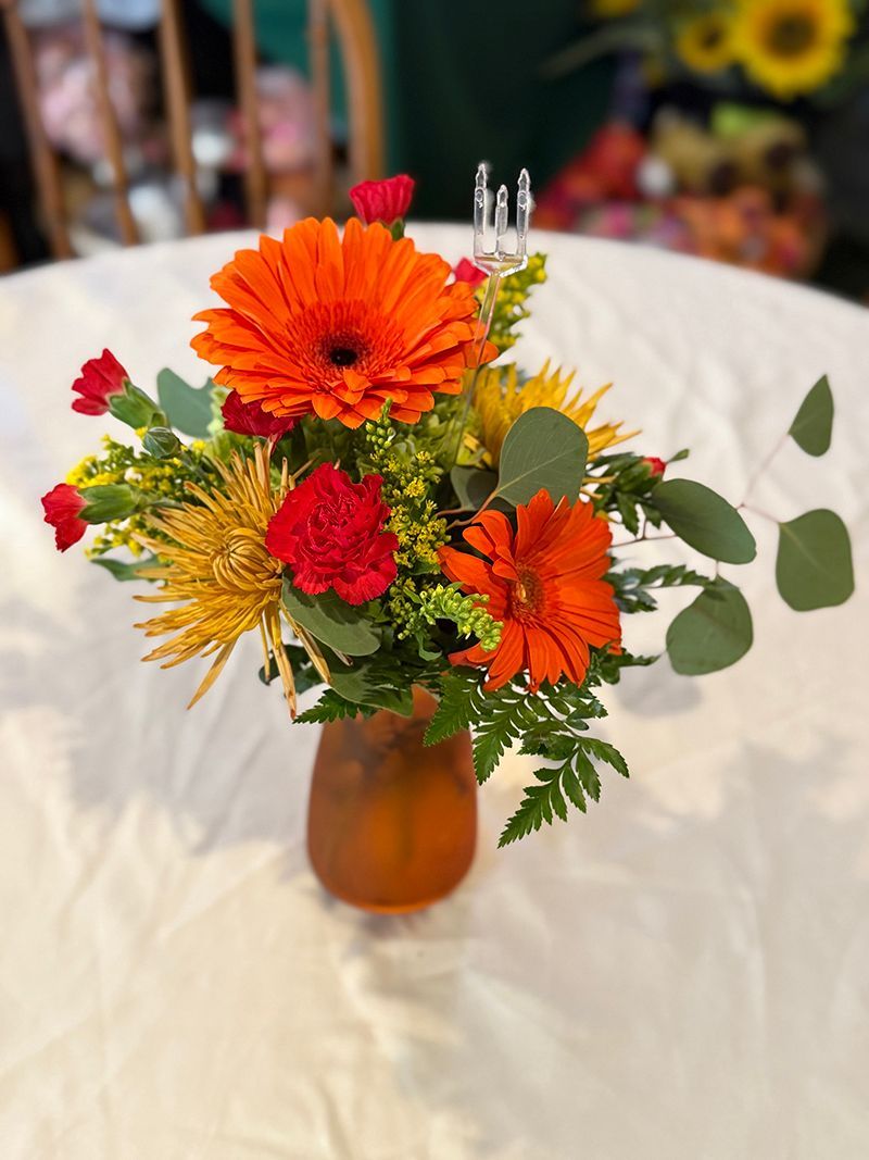 Orange floral arrangement in an orange vase on a white tablecloth, featuring gerbera daisies and carnations.