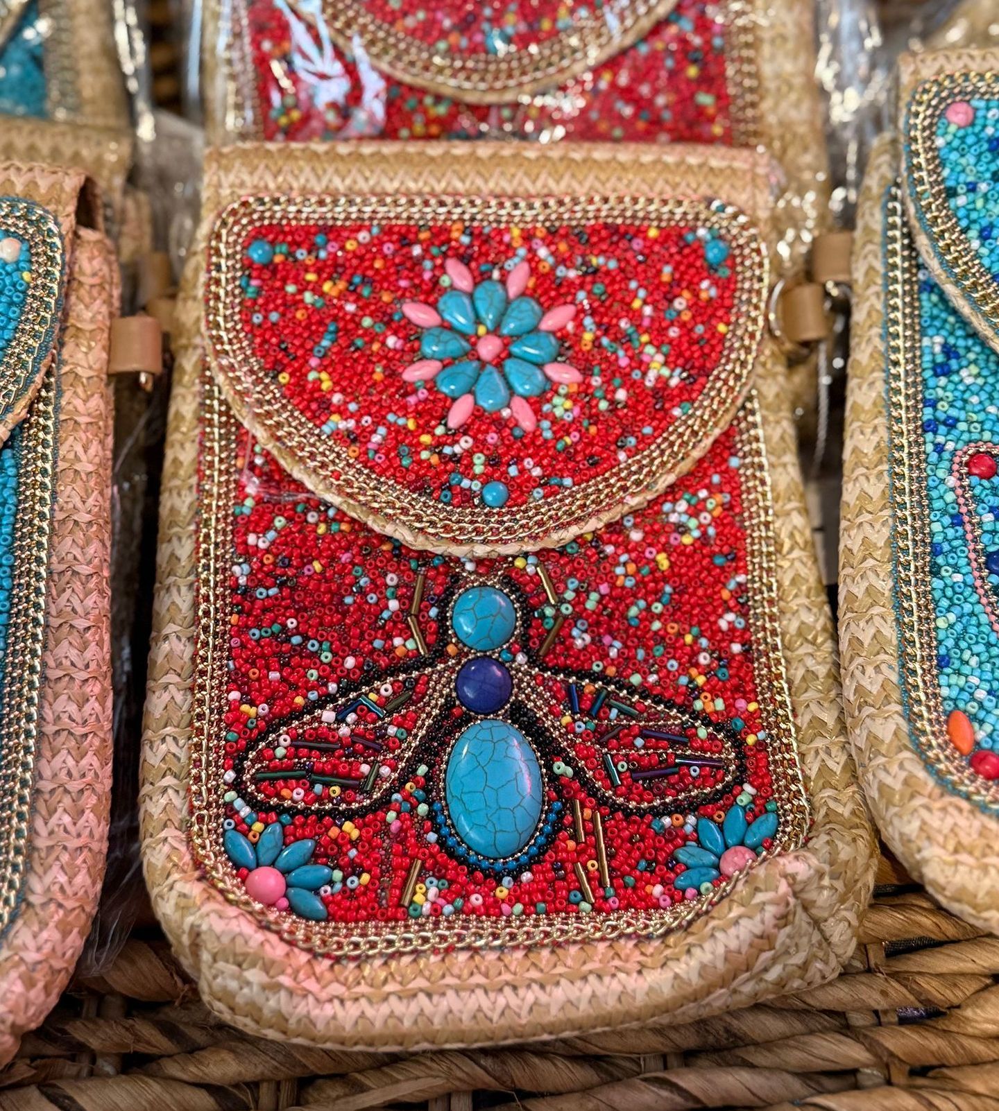 Close-up of several beaded bags, including one red with a turquoise bee design and others in gold and blue.