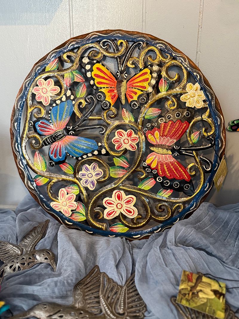 A cone filled with flowers and ferns is hanging on a wall next to potted plants.