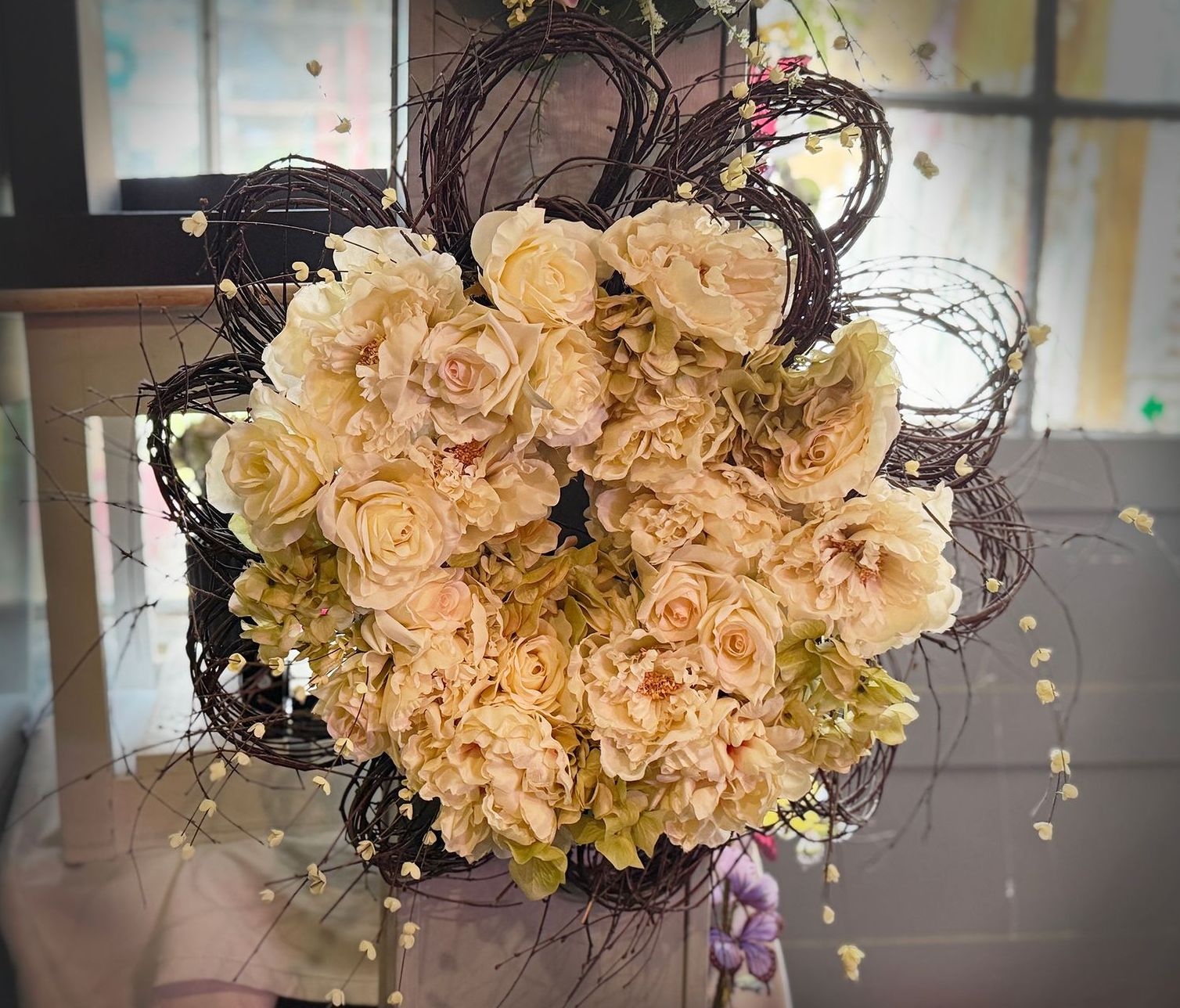 A floral arrangement featuring cream-colored roses and peonies, encircled by a woven, dark-brown vine design.