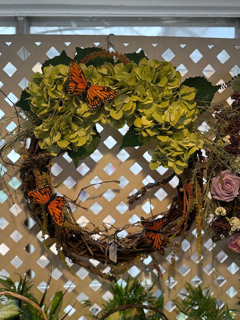 Wreath with green flowers and orange butterflies, hanging on a white lattice.