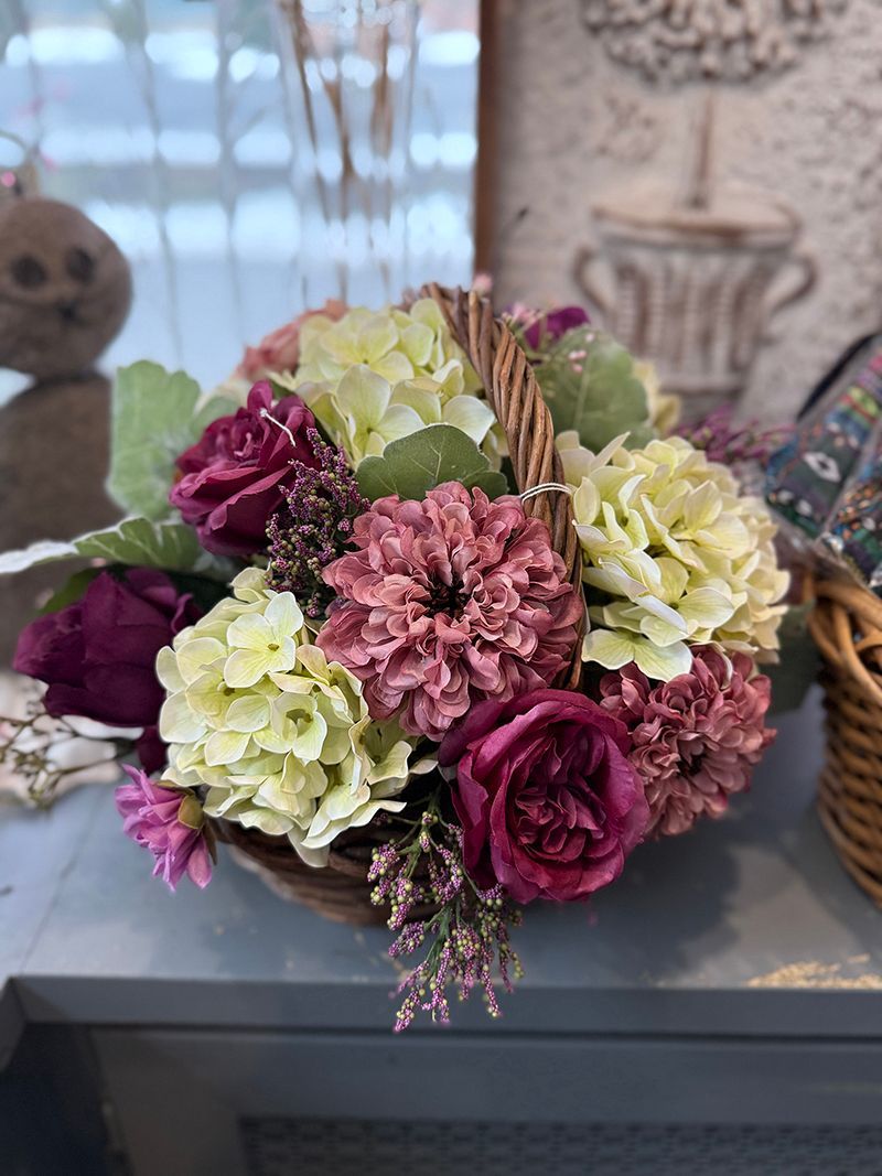 Basket of pink, burgundy, and light green flowers on a gray surface.