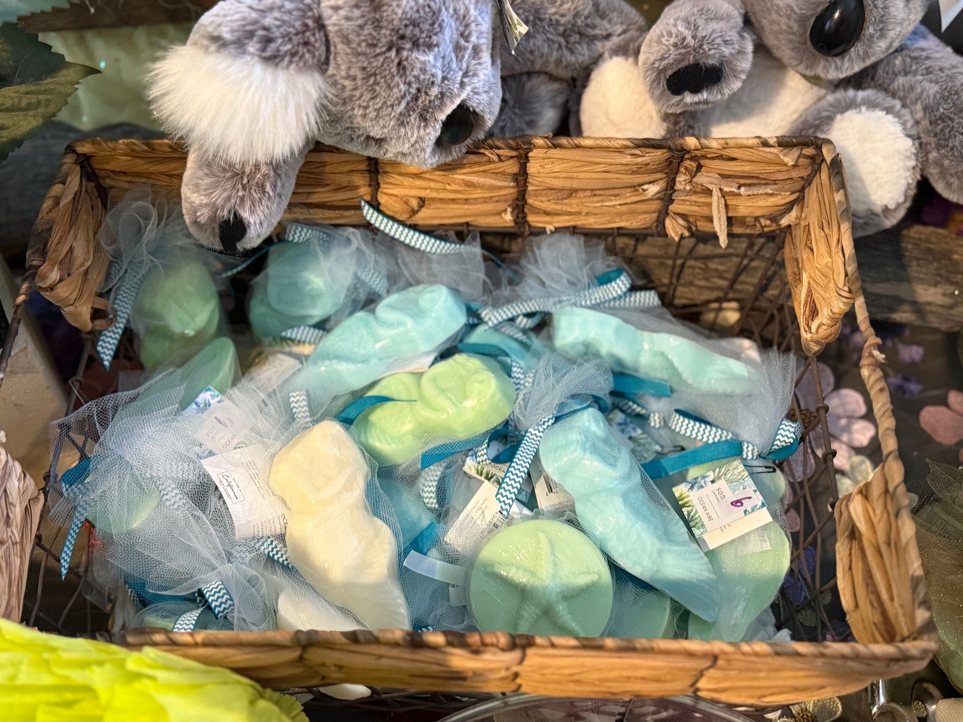 Basket of assorted pastel-colored soaps wrapped in blue netting. Koala plushies are visible above the basket.