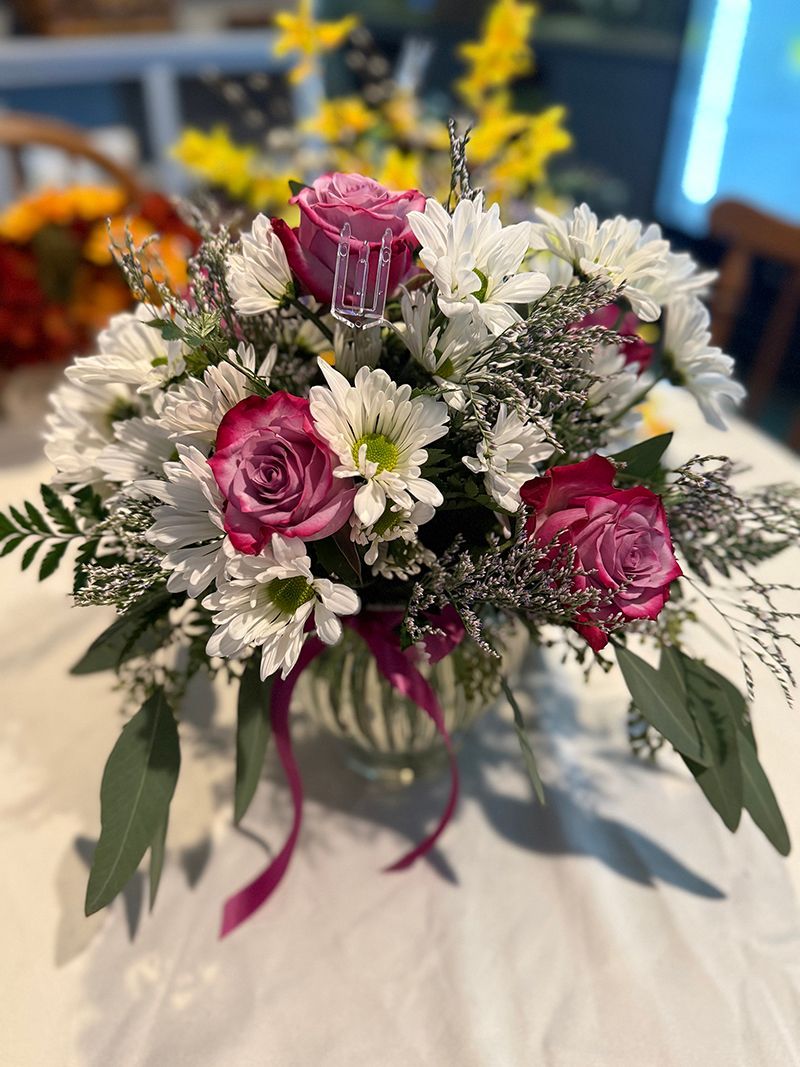 Floral arrangement in a glass vase with pink roses, white daisies, and greenery.