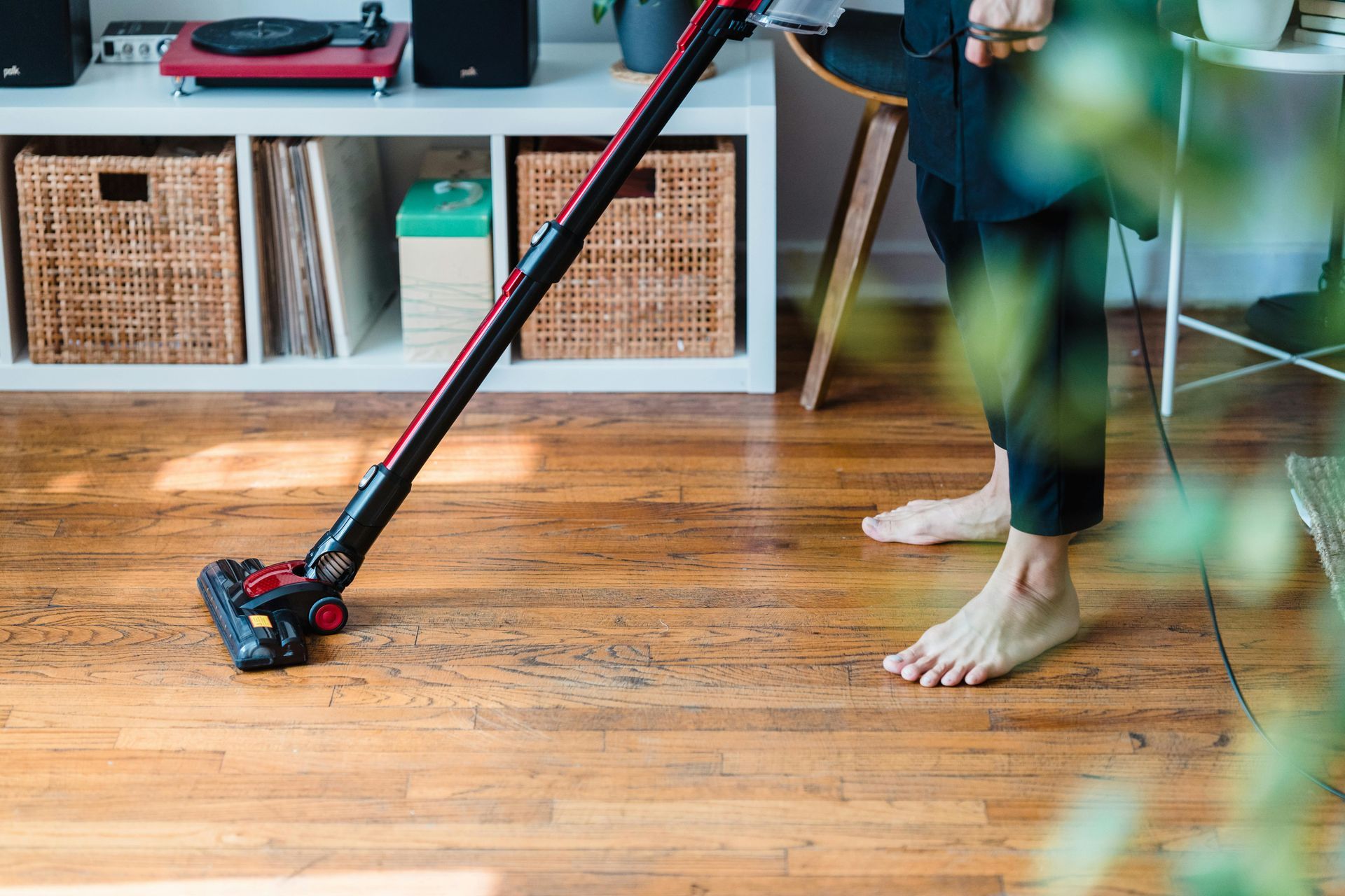 A person is using a vacuum cleaner on a wooden floor in a living room.