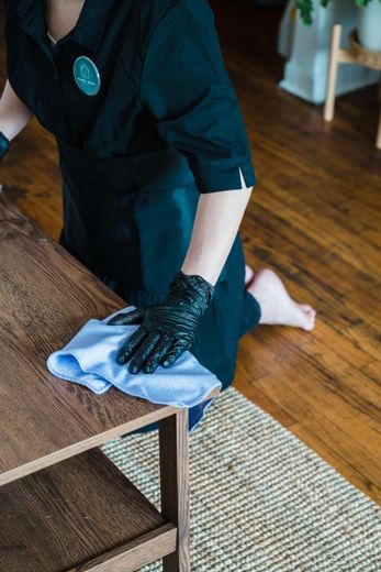 A woman wearing black gloves is cleaning a wooden table with a cloth.