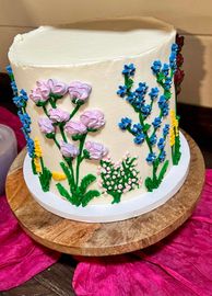 A cake with flowers on it is sitting on a wooden cutting board.