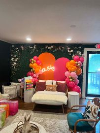 A living room decorated for a baby shower with balloons and a neon sign.