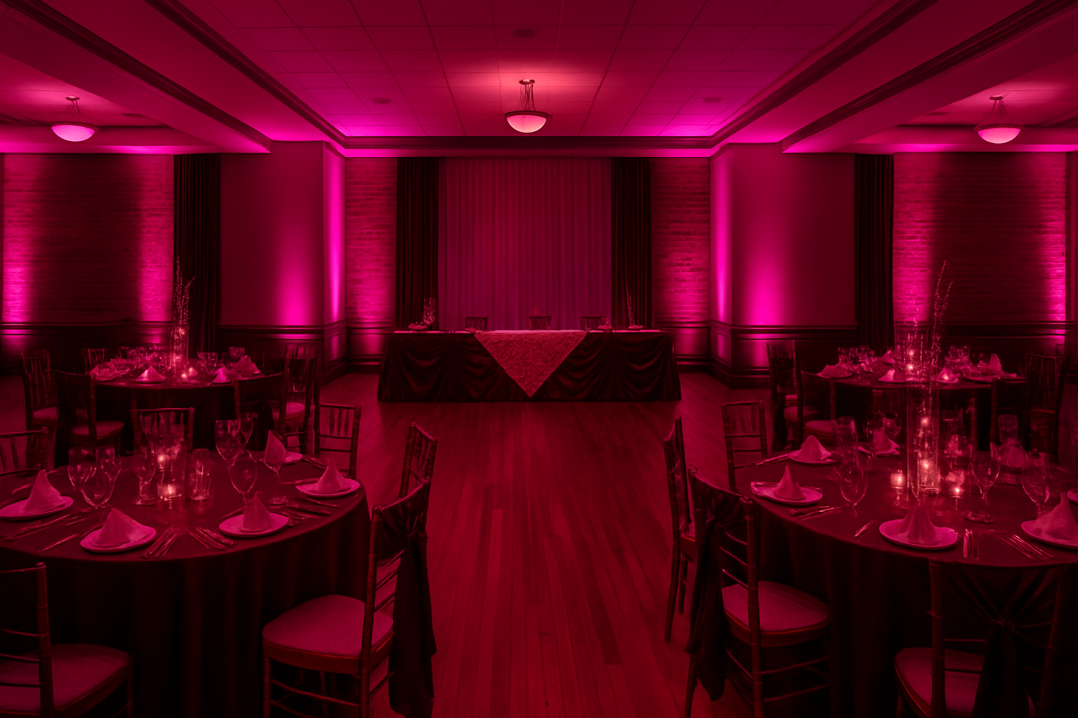 Pink-lit banquet hall with round tables set for a formal event. Stage in the background.