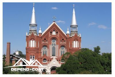 A large red brick building with two silver towers and a cross on top.