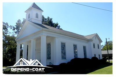 A white church with a gray roof is sitting in the middle of a grassy field.