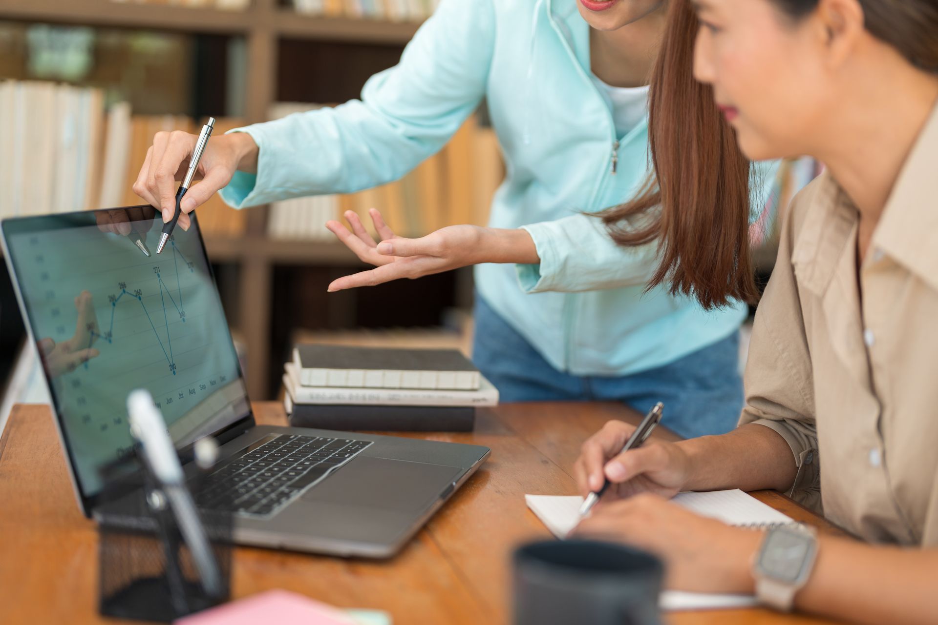Dos mujeres están sentadas en una mesa mirando una computadora portátil.