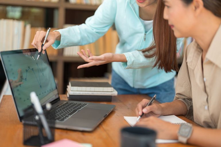 Dos mujeres están sentadas en una mesa mirando una computadora portátil.