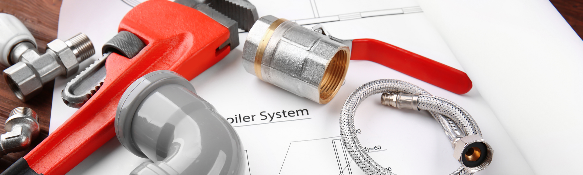 Plumbing tools and parts arranged on a white surface, including a red pipe wrench, metal fittings, and a flexible hose.