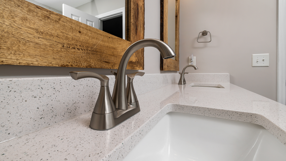 Bathroom sink with silver faucet, white countertop, and large wooden-framed mirror.