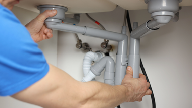 Person connecting gray pipes under a sink.